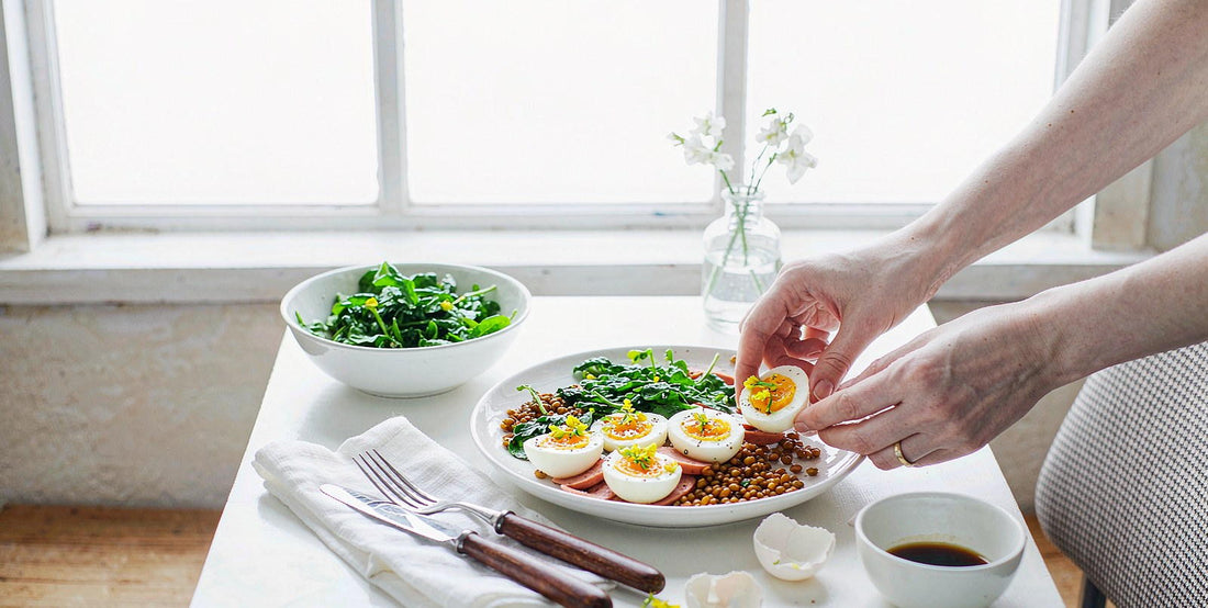 Fair-skinned hands arranging eggs, greens, and lentils on a bright dining table for a balanced daily diet.