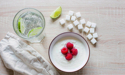 Overhead flat lay of sparkling water with lime, raspberry yogurt and a few sugar cubes