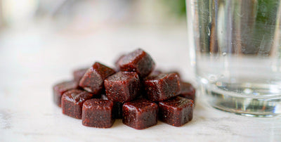 Dark reddish grass-fed beef liver gummies beside a glass of water on a white marble counter