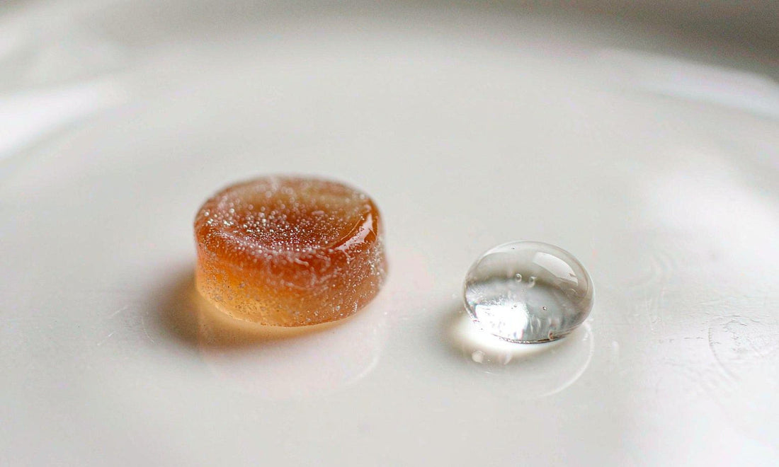 Extreme macro of a plain unlabeled supplement gummy and a clear water drop on a bright white surface