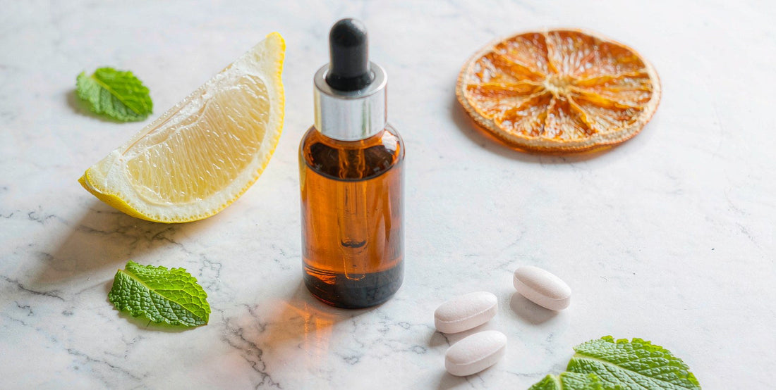 A plain unlabeled amber dropper bottle and pale capsules on a bright marble surface with a sliced lemon