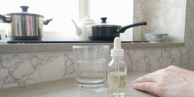 Plain unlabeled glass dropper bottle with water on a bright kitchen counter in daylight