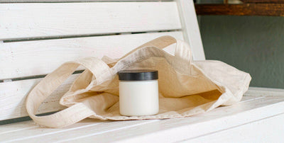 Plain white supplement jar resting in a canvas tote bag on a sunlit white wooden bench