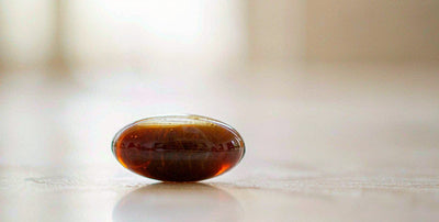 Macro close-up of a single amber beef liver supplement capsule on a bright clean surface