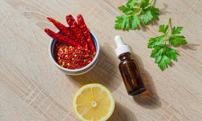 Overhead flat lay of dried cayenne peppers, chilli flakes and a dropper bottle on pale oak
