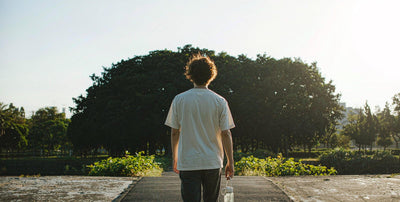 Fair-skinned person from behind walking in a sunny park holding a water bottle
