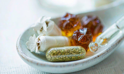 Capsules, gummies, and a liquid dropper arranged on a light ceramic spoon in soft daylight