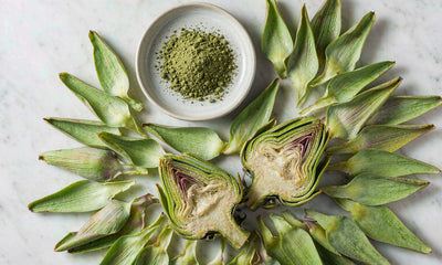 Top-down flat lay of fresh artichoke leaves and hearts with green leaf powder in a dish