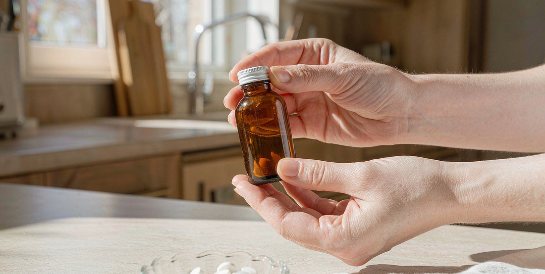 Fair-skinned hands holding a plain unlabeled supplement bottle on a bright kitchen counter in morning light.