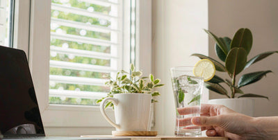 Bright office desk with a hand holding a glass of water and lemon, calm support routine after work