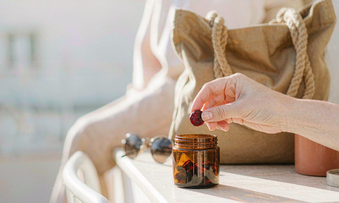 A hand reaching into an amber jar of gummies beside a canvas tote bag on a stone ledge