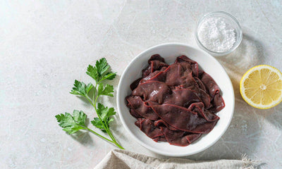 Top-down flat lay of sliced beef liver with parsley, lemon and coarse salt on pale stone