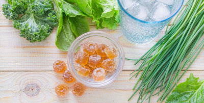 Grass-fed beef liver gummies in a bowl with water and greens on a bright kitchen board