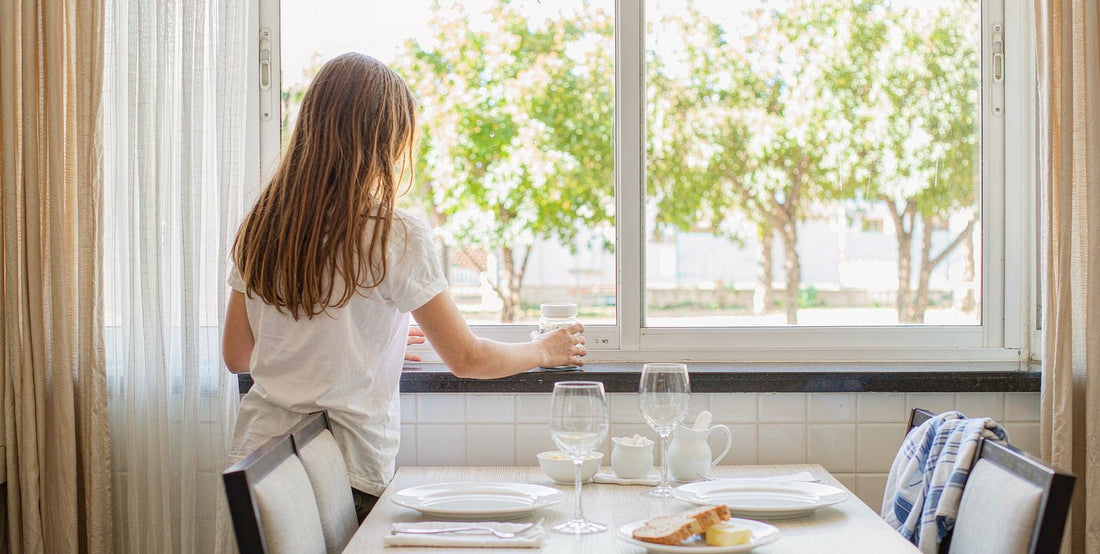 Bright airy kitchen scene with a person seen from behind at a sunny window