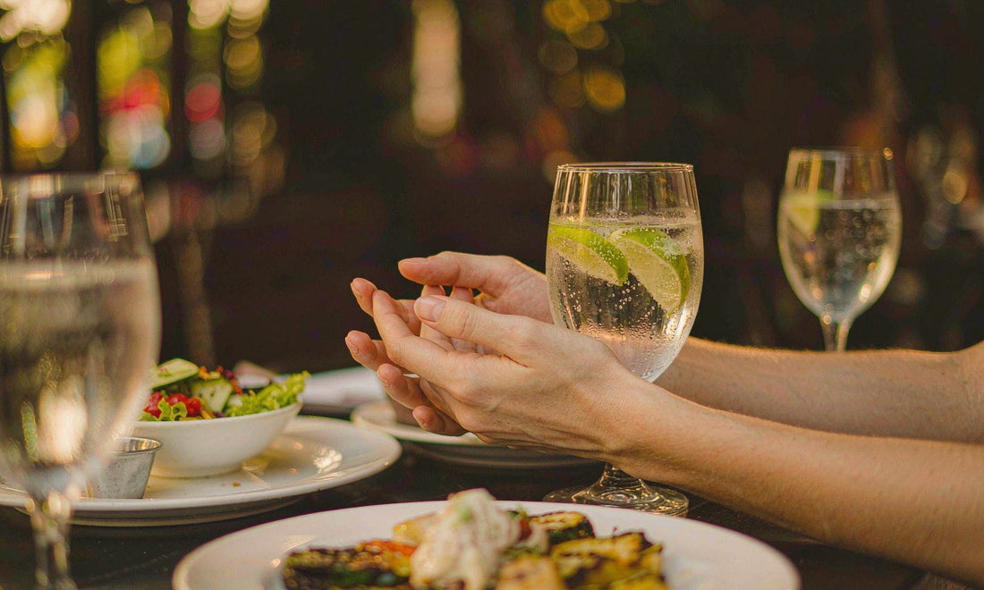 Fair-skinned hands beside a sparkling water with lime at a warmly lit restaurant table