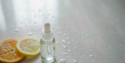 Plain unlabeled dropper bottle beside fresh citrus slices and water droplets on a light surface