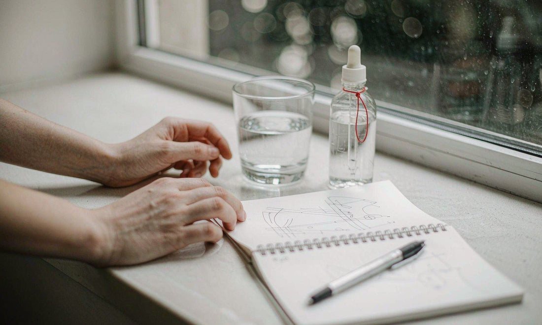 Bright kitchen counter at dusk with a dropper bottle, water glass and an open habit journal