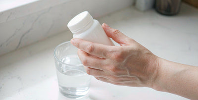 Western fair-skinned hands holding a plain unlabeled supplement bottle and a glass of water