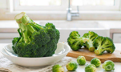 A bowl of broccoli and Brussels sprouts on a bright kitchen table in soft natural light, no people