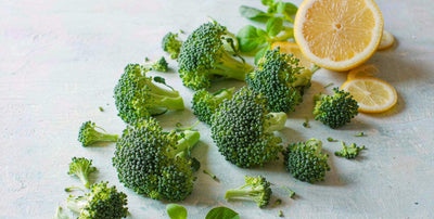 Fresh broccoli florets and a halved lemon arranged as a bright flat-lay on a light wooden board