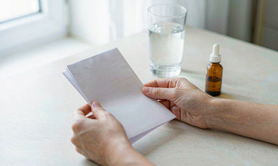 Fair-skinned hands holding a folded lab report beside an amber dropper bottle and a glass of water