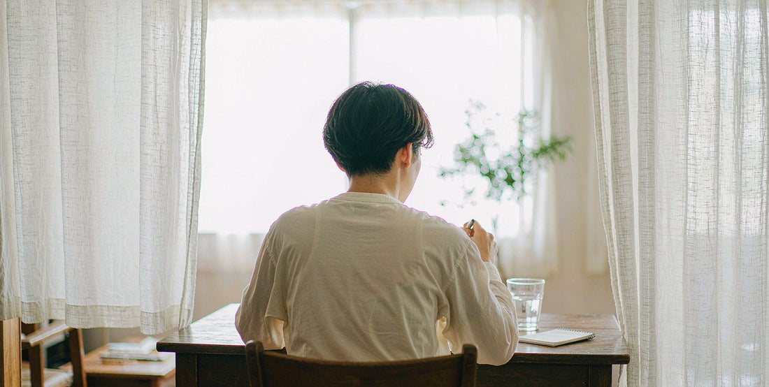 A fair-skinned person seen from behind at a desk with a glass of water and a written notepad